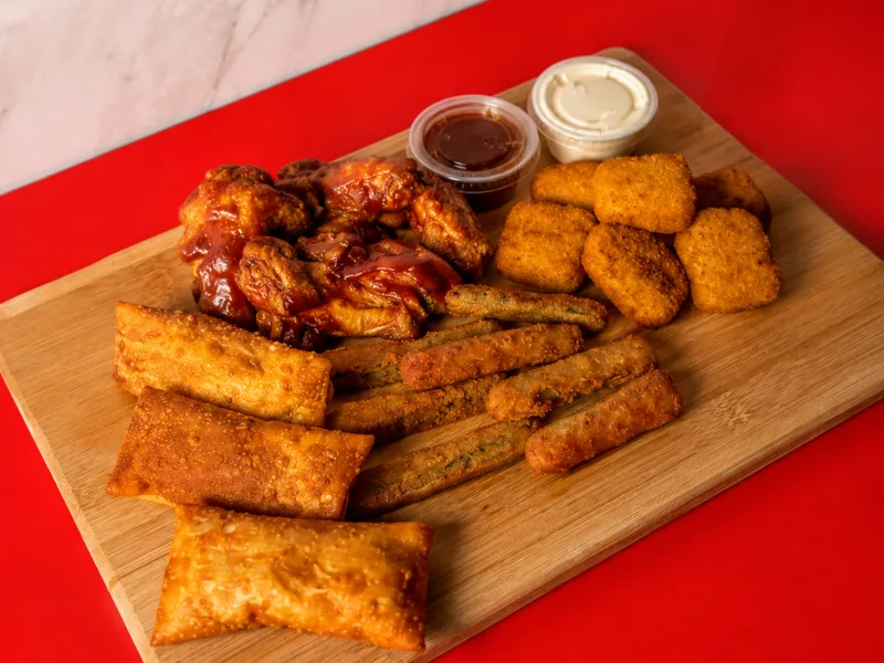 Chicken wings, nuggets, egg rolls and fried zucchini on a wooden board with two dipping sauces