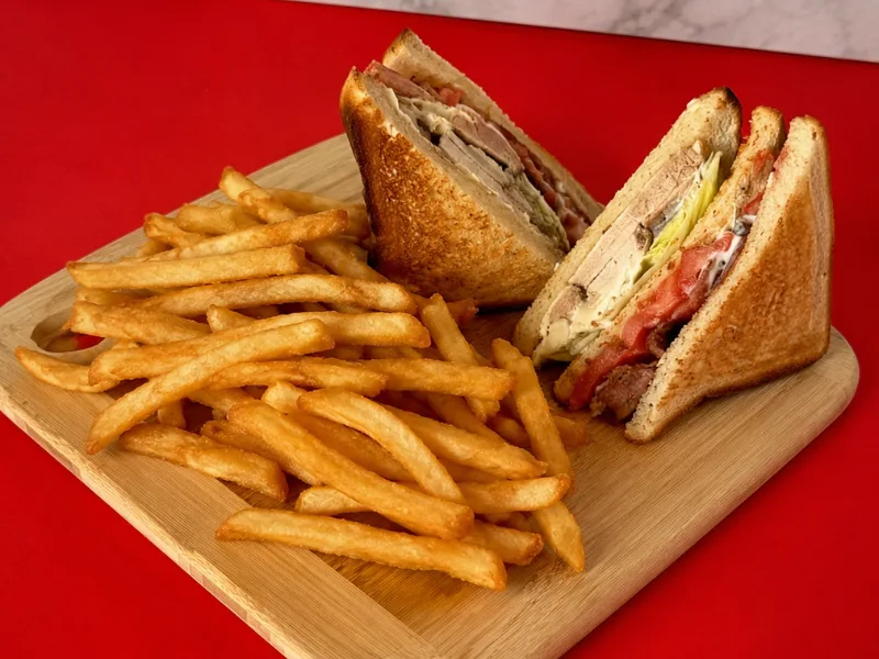 A club sandwich cut into quarters with a pile of french fries